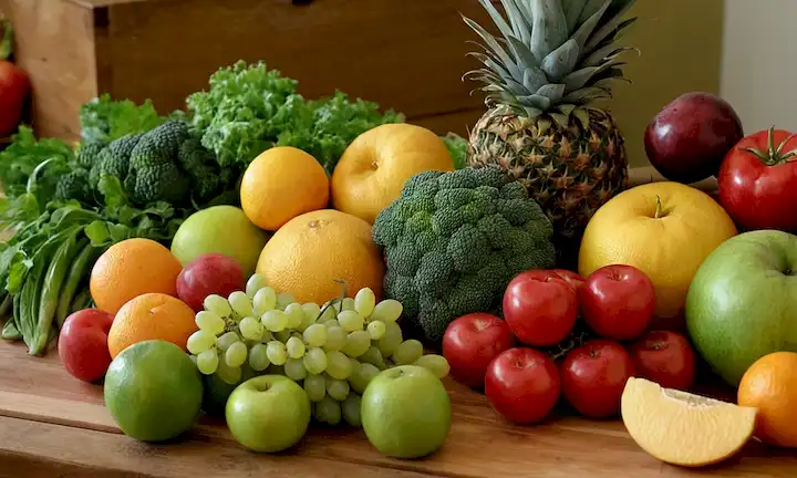 Disposición colorida de frutas y verduras frescas en una mesa de madera, con colores vibrantes y texturas naturales, mostrando variedad y abundancia, posiblemente con unas pocas perchas o pequeños contenedores para mayor encanto